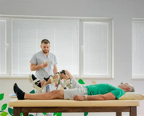 Квалифициран рехабилитатор извършва пасивно раздвижване на долен крайник на пациент с помощта на апарат Artromot.
