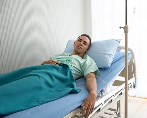 Млад мъж пациент, лежащ в болнично легло по време на престой или лечение в болница.